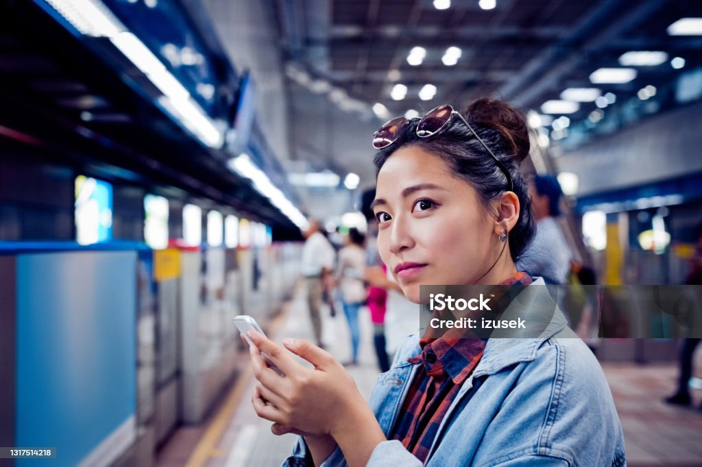 Woman with mobile phone at subway station Beautiful young woman looking away. Female is holding smart phone. She is at subway station. 20-24 Years Stock Photo
