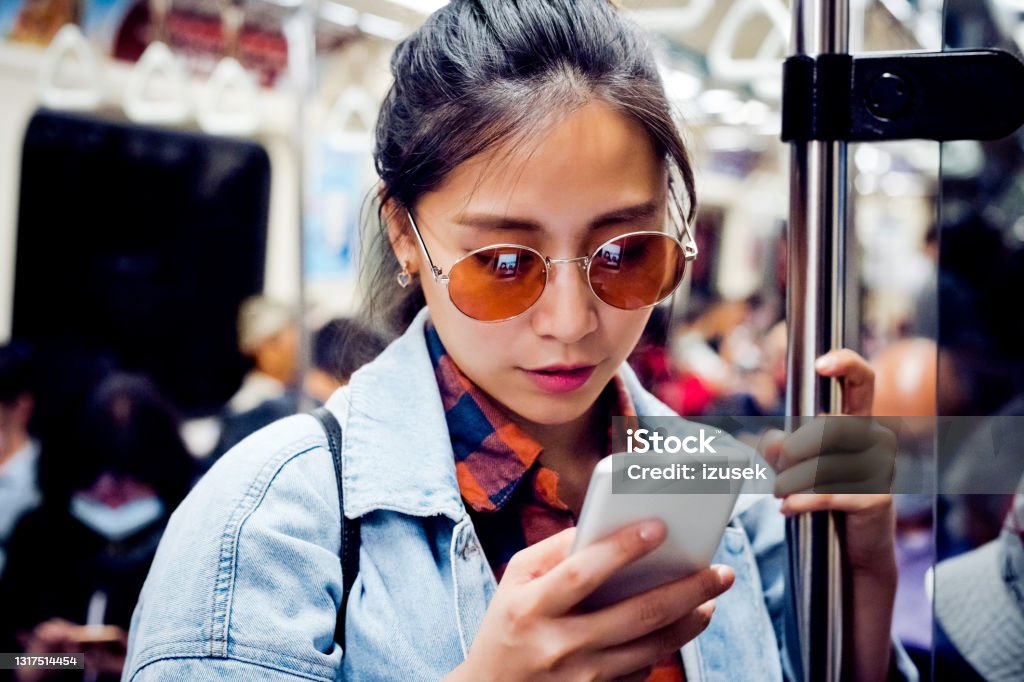 Woman using mobile phone in subway train Young woman text messaging through phone. Beautiful female is using smart phone in subway train. She is wearing sunglasses. Subway Train Stock Photo