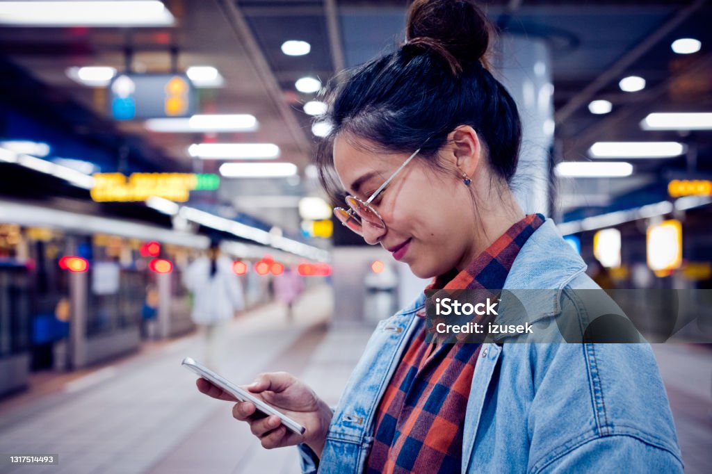 Woman using mobile phone at subway station Fashionable young woman using smart phone. Beautiful female in sunglasses is smiling. She is at subway platform. Human Face Stock Photo