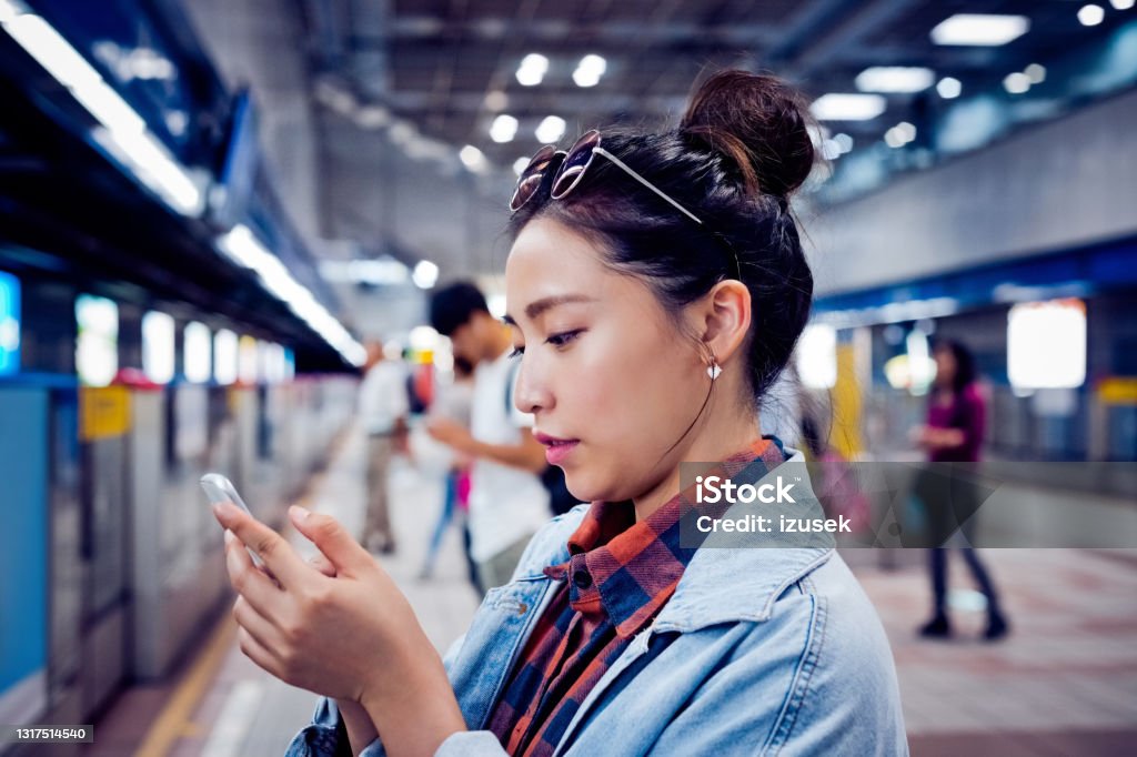 Woman using mobile phone at subway platform Young woman text messaging through phone. Beautiful female is using smart phone. She is at subway station. 20-24 Years Stock Photo