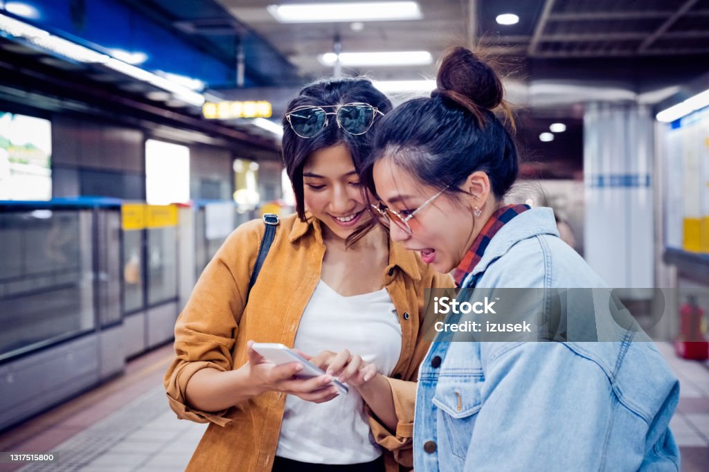 Friends discussing over phone at subway station Young women looking in smart phone. Female friends are exploring city during weekend. They are at subway station. 20-24 Years Stock Photo