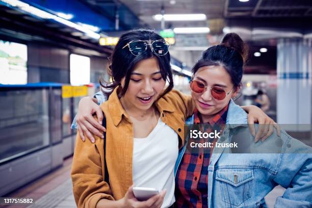 Females Discussing Over Phone At Subway Station Stock Photo - Download Image Now - Subway, 20-24 Years, Adult