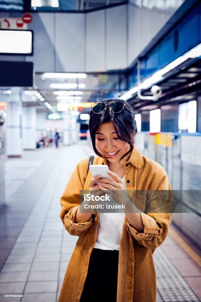 Female using mobile phone at subway station Smiling young woman text messaging through phone. Happy female is using smart phone. She is at subway station. 20-24 Years Stock Photo
