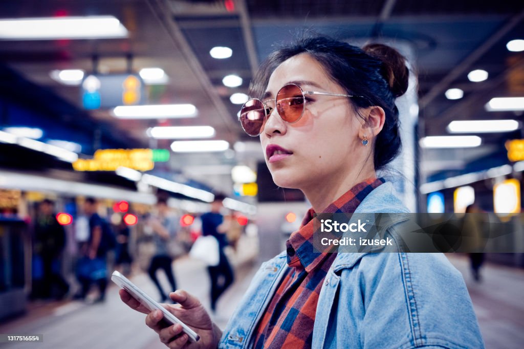 Fashionable young woman at subway station Fashionable young woman looking away. Beautiful female in sunglasses is holding smart phone. She is at subway station. 20-24 Years Stock Photo