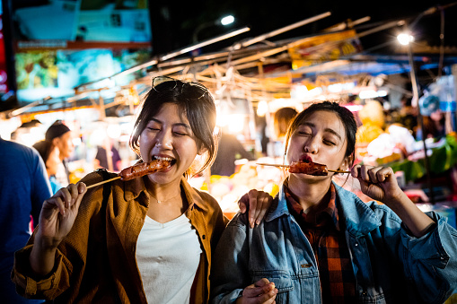 Young women enjoying street food at night. Females are spending leisure time together in city. They are wearing casuals.