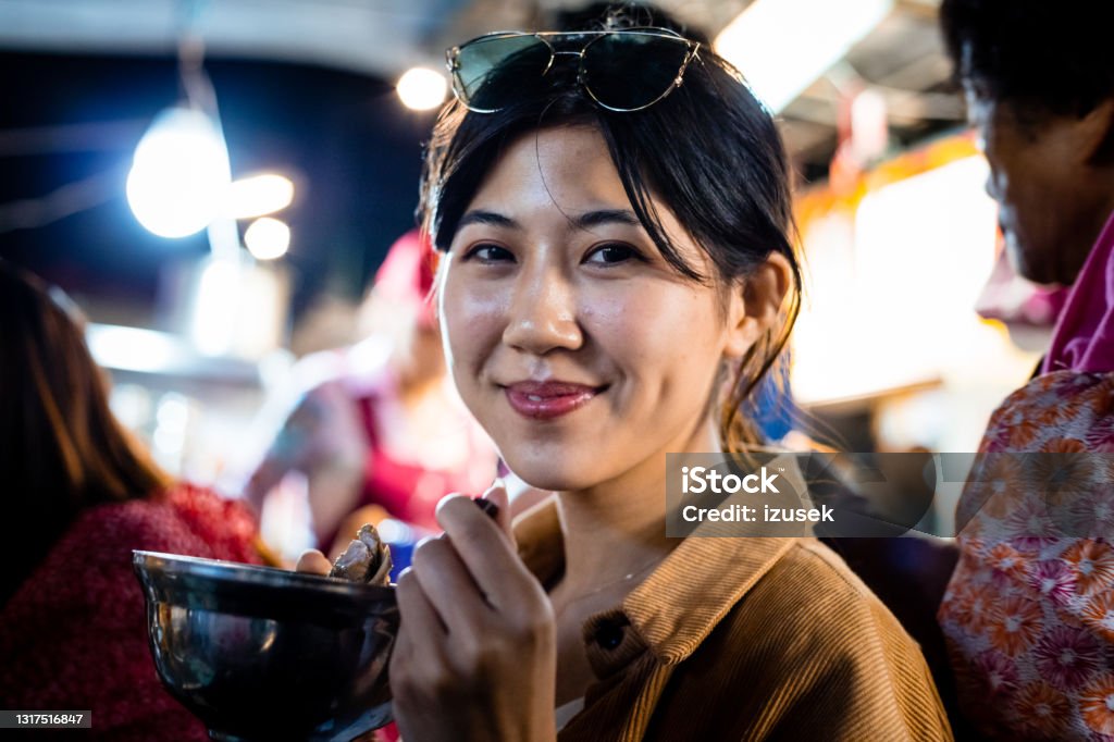 Smiling woman eating food at night Portrait of smiling woman eating food. Beautiful young female is spending leisure time. She is in city at night. Night Market Stock Photo