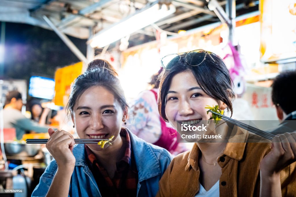 Happy female friends eating street food at night Portrait of smiling women eating street food. Happy young females are spending leisure time together. They are holding chopsticks. Happiness Stock Photo