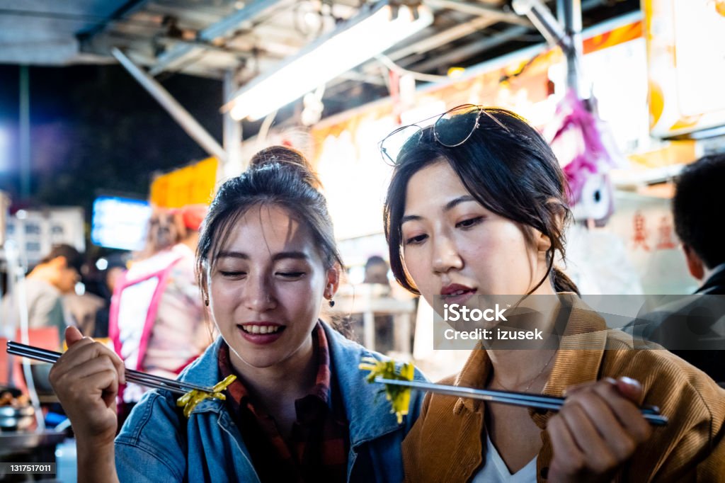 Female friends eating street food at night Women eating street food at night. Young females are spending leisure time together. They are enjoying city break. 20-24 Years Stock Photo
