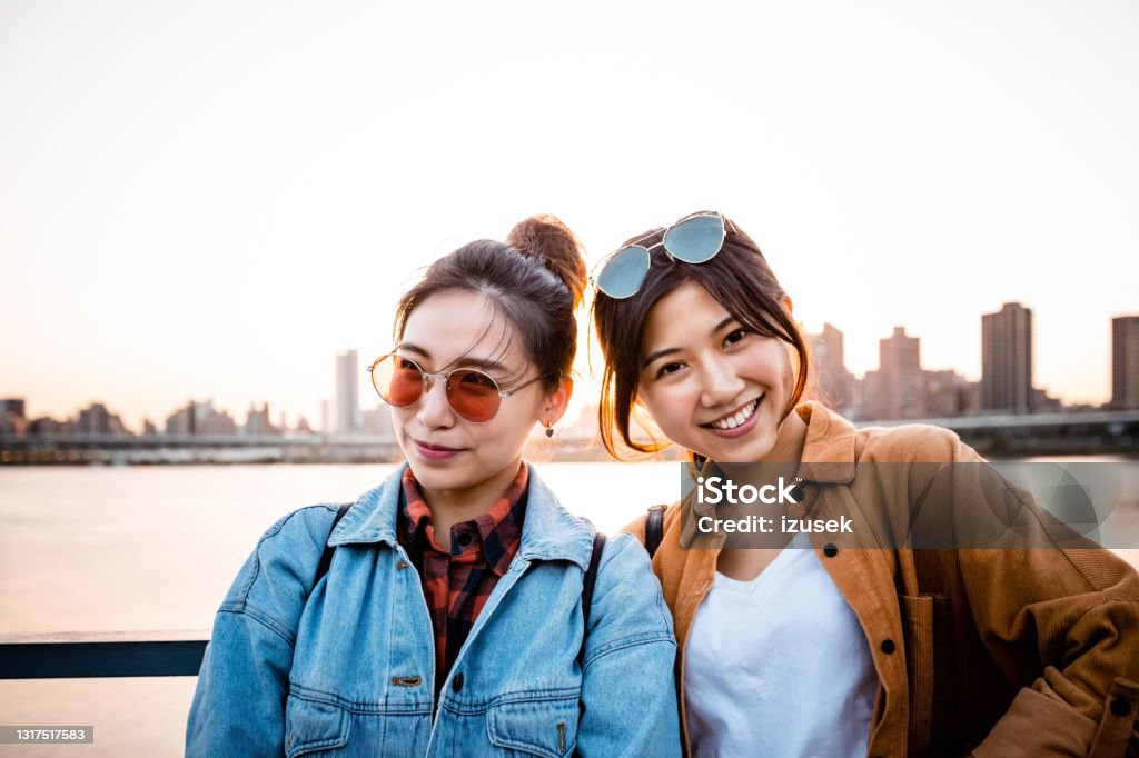 Young female friends on city break Smiling beautiful women smiling on city break. Young female friends are wearing casuals. They are standing against river during sunset. 20-24 Years Stock Photo