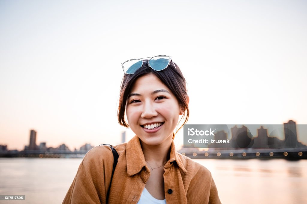 Smiling woman against river in city during sunset Portrait of happy woman during sunset. Beautiful young female is against sky during sunset. She is in city. 20-24 Years Stock Photo