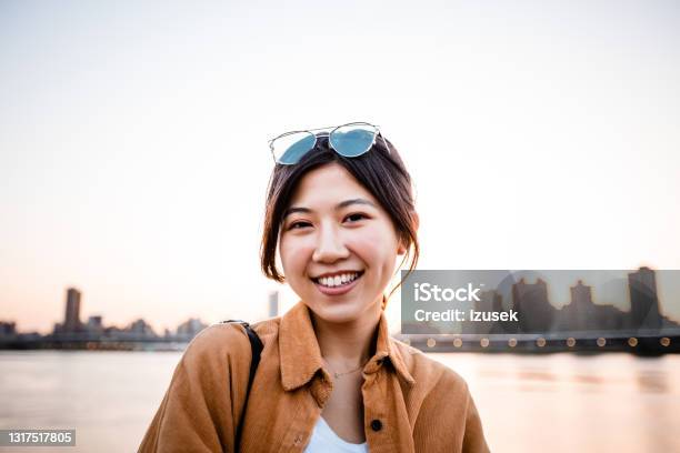 Smiling Woman Against River In City During Sunset Stock Photo - Download Image Now - 20-24 Years, Adult, Adults Only