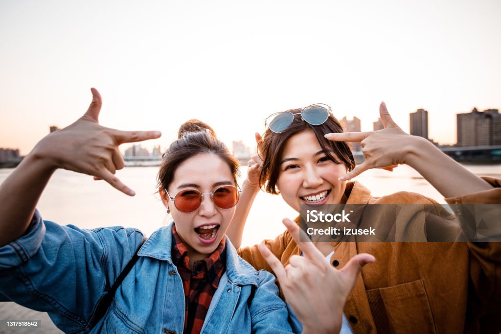 Carefree female friends enjoying city break Portrait of cheerful female friends gesturing. Carefree young women are enjoying city break. They are showing horn signs. 20-24 Years Stock Photo
