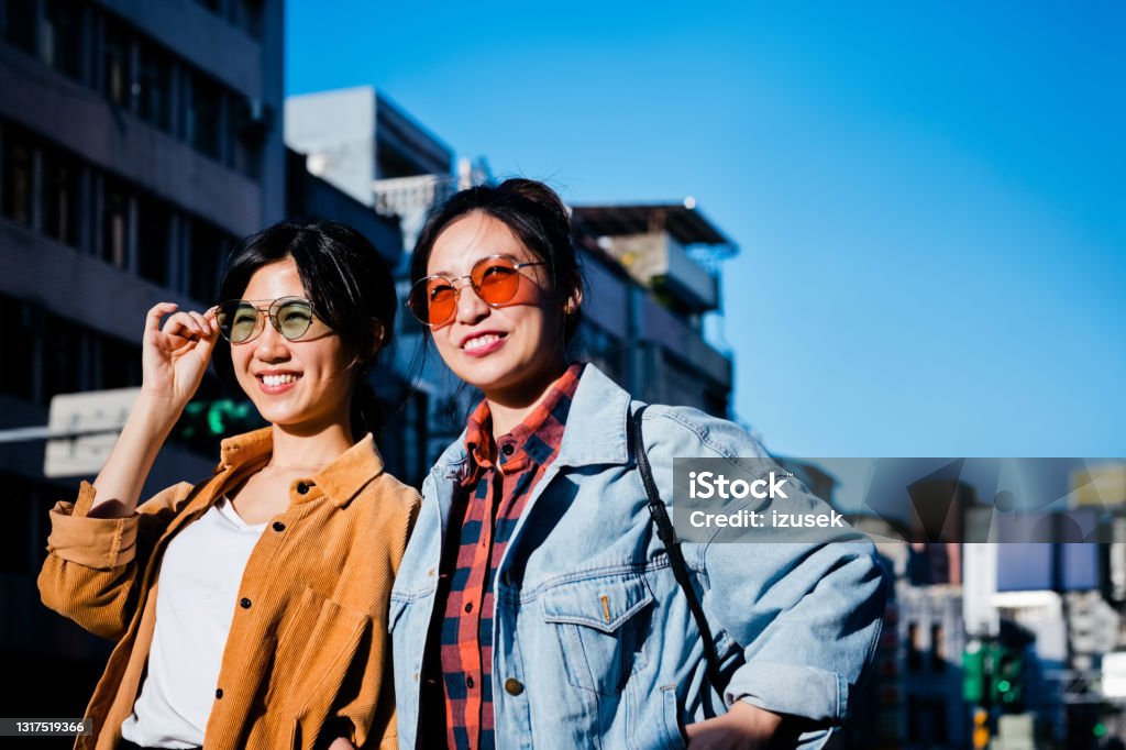 Young female friends in city during sunny day Cheerful beautiful young women looking away. Female friends are on city break during weekend. They are wearing sunglasses on sunny day. 20-24 Years Stock Photo