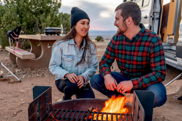 istock Young Multi-Ethnic Couple Out Camping, Warming Themselves By The Campfire, Talking An Enjoying The Evening 1317519595