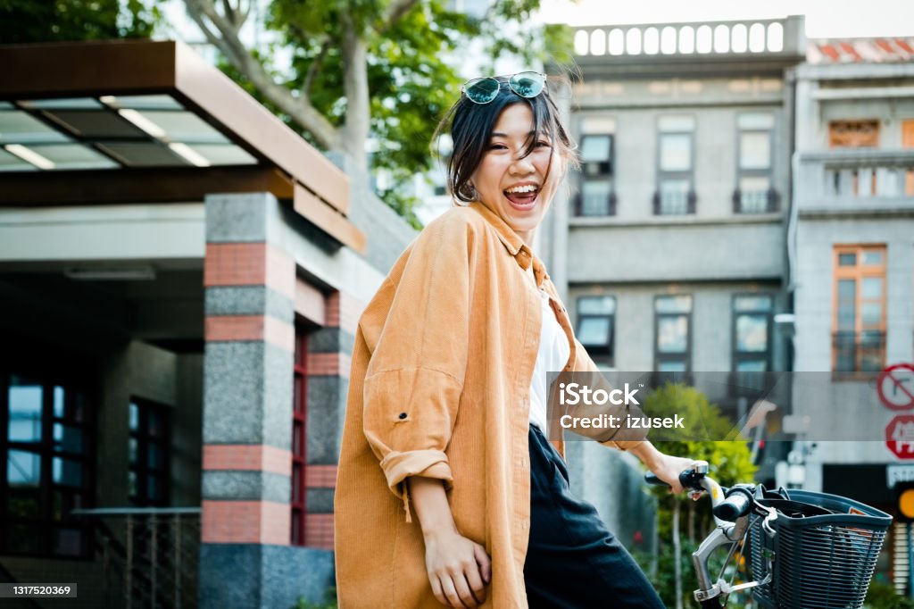 Cheerful woman with bicycle in city Portrait of happy woman cycling in city. Young female with bicycle is outside buildings. She is enjoying weekend. 20-24 Years Stock Photo