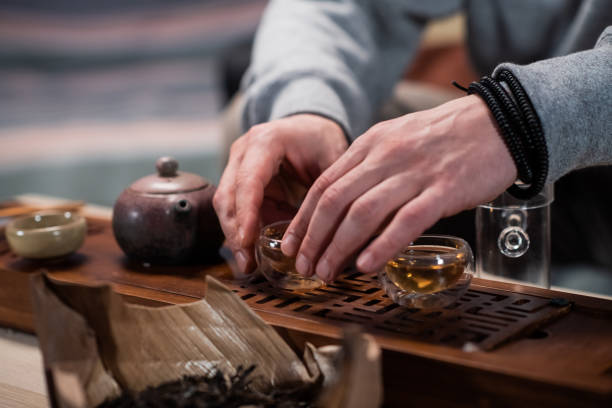 un maître oriental organise une cérémonie du thé pour un visiteur d’un salon de thé. plan rapproché avec un ensemble de thé et un plateau en bambou - tea chinese tea heat teapot photos et images de collection