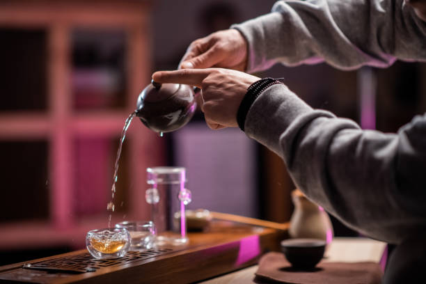 plan rapproché avec les mains d’un maître de cérémonie de thé dans un magasin de thé, versant le thé pour la dégustation dans des tasses spéciales sur une table en bambou avec un plateau - chinese tea photos et images de collection