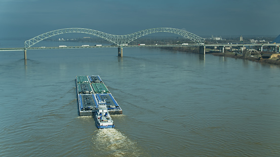 Drone shot of a barge on the Mississippi, approaching the Hernando de Soto Bridge connecting Tennessee and Arkansas.