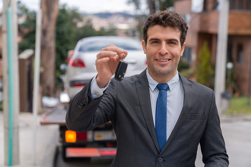 Portrait of a Latin American salesman delivering a car to your home while holding the keys and looking at the camera smiling