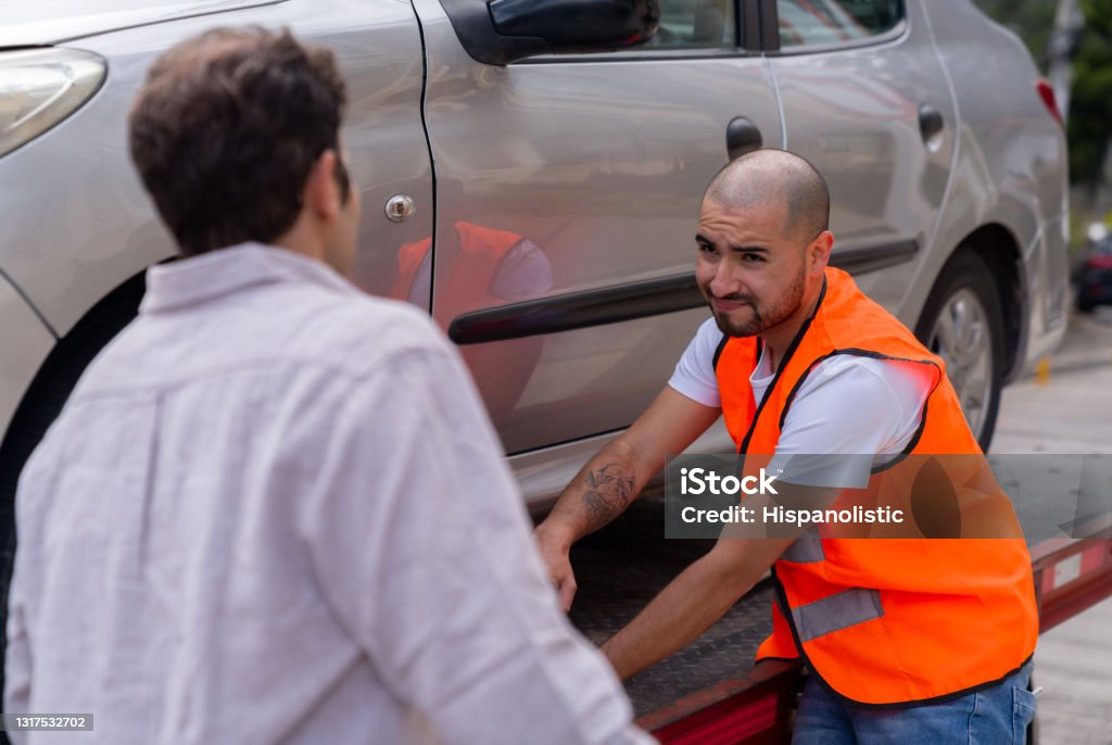 Tow truck operator towing a car and feeling sorry for the owner Latin American tow truck operator towing a car and feeling sorry for the owner - roadside assistance concepts Tow Truck Stock Photo