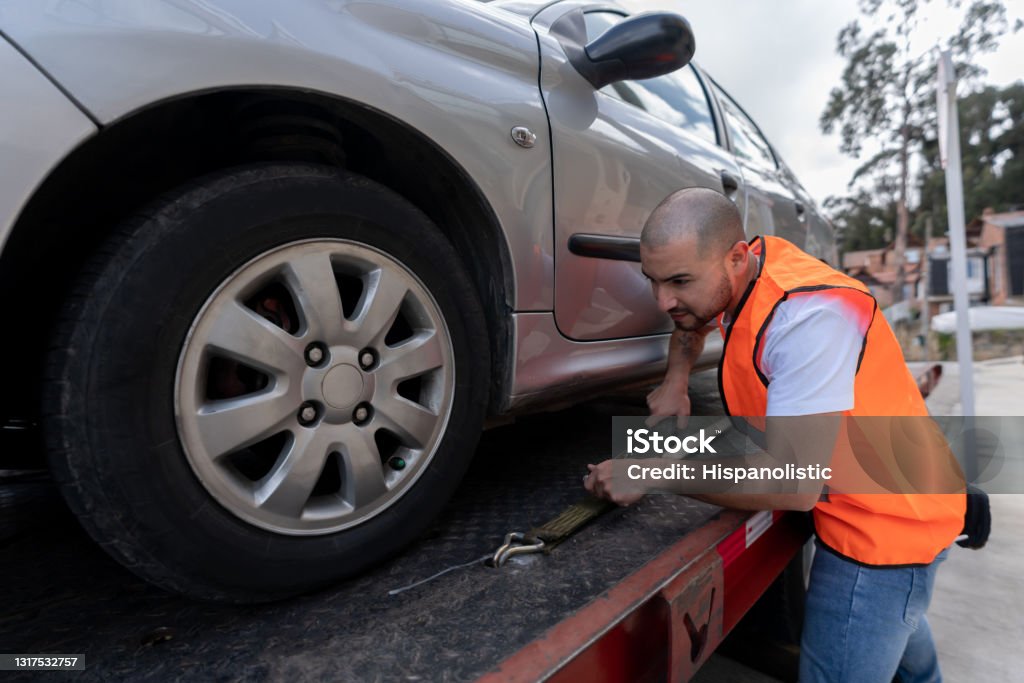 Latin American tow truck operator towing a car Latin American tow truck operator towing a car - roadside assistance concepts Tow Truck Stock Photo
