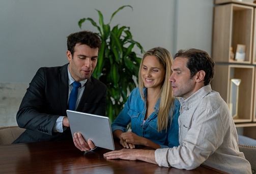 Latin American couple in a meeting with their real estate agent looking at pictures of a property on a tablet computer - business concepts