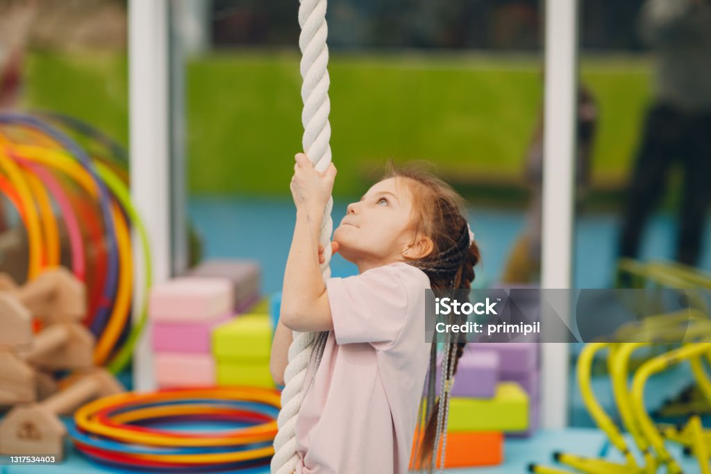 Kids doing exercises climbing tightrope in gym at kindergarten or elementary school. Children sport and fitness concept. Kids doing exercises climbing tightrope in gym at kindergarten or elementary school. Children sport and fitness concept Child Stock Photo