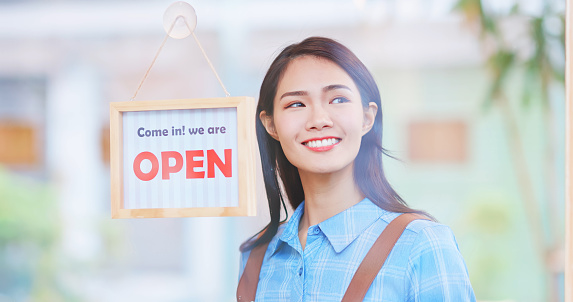 Pretty asian female shop owner flipping open sign in the morning and look around expecting customers