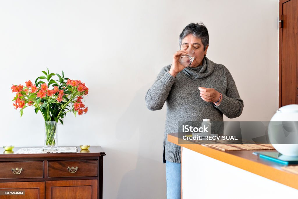 Latin old woman taking medicine at home elderly Latina between 60-69 years taking medication at home Vitamin Stock Photo