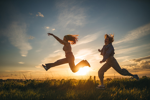 Two girls are jumping happily. In the background is the sunset