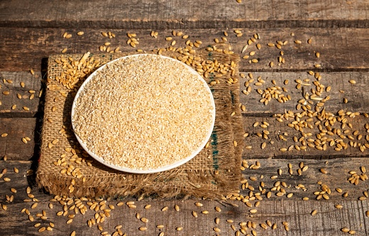 Closeup of Uncooked Cracked Wheat or Dalia in a Plate on Burlap Fabric Isolated on Wooden Background in Horizontal Orientation.