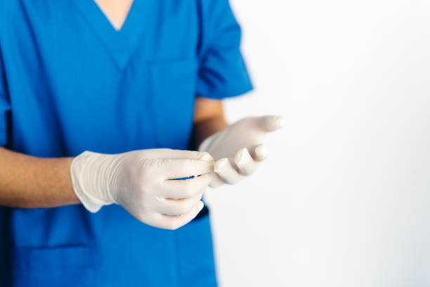 Close up of doctor's hands putting on blue sterilized surgical gloves in the medical clinic. Protective Glove, Surgical Glove, Protective Workwear, Getting Dressed, Safety putting on latex gloves stock pictures, royalty-free photos & images