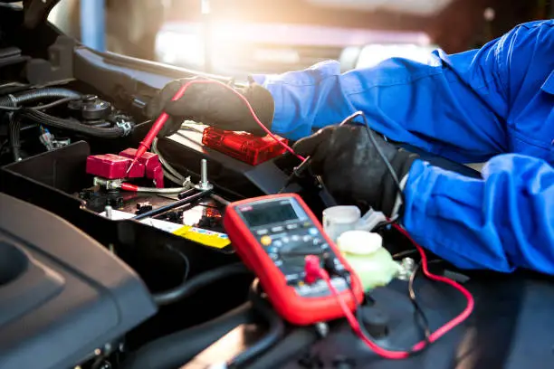 Photo of Technician uses multimeter voltmeter to check voltage level in car battery. Service and Maintenance car battery.