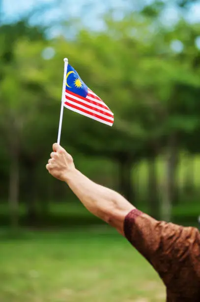 Closed up hand of person holding Malaysia Flag in the park.
