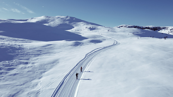 Active couple cross country skiing on a slope through wild snowy mountain wilderness on a clear cold winters day.