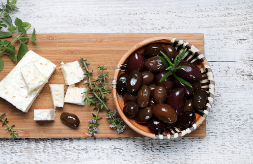 Black olives, feta cheese and aromatic herbs on wooden cutting board. Directly above.