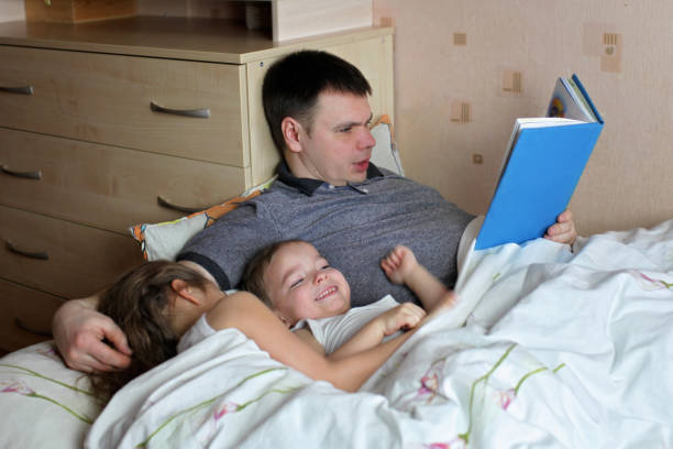 istock Happy children lying in bed with their father who is reading a book 1317563534