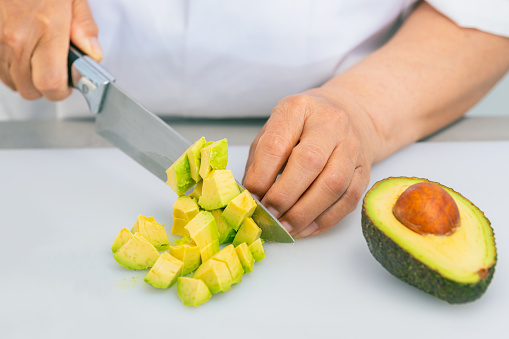 Tasty looking avocado freshly cut into dice using a kitchen knife on a cutting board. Selective focus and close up. Cooking and healthy food concept.