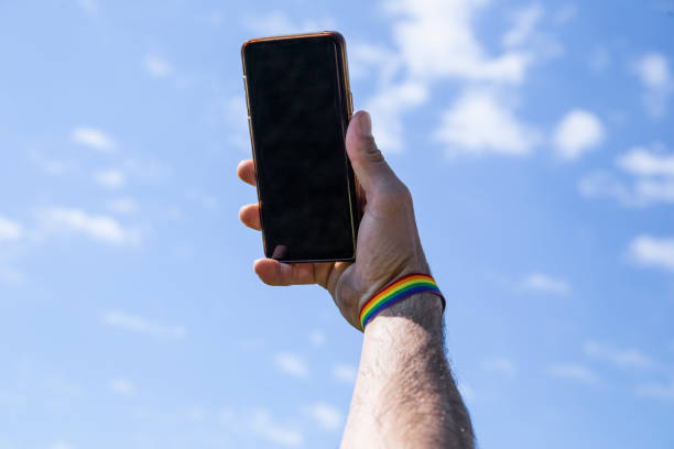 istock hand up using the mobile with a lgtb colored bracelet with the sky in the background. 1317569309