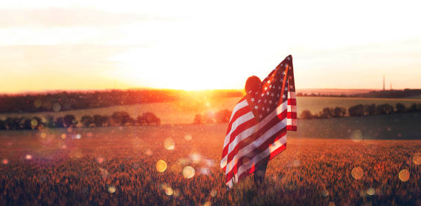 Independence Day. Beautiful young woman with the American flag in a wheat field at sunset with bokeh and sparkle. 4th of July. Independence Day. Beautiful young woman with the American flag in a wheat field at sunset with bokeh and sparkle. 4th of July military lifestyle stock pictures, royalty-free photos & images