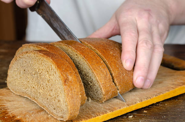 istock Hands slice bread on a wooden cutting board. 1317571464