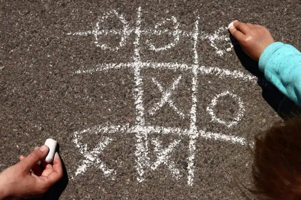 child plays with his mother in tic-tac-toe chalk on the asphalt
