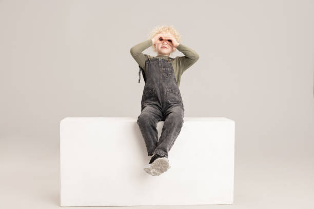 istock One Caucasian little boy sitting on box isolated over gray studio background. 1317583856