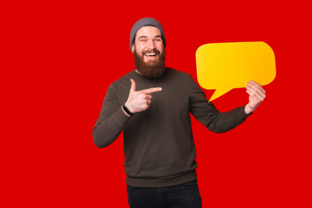istock Cheerful young bearded hipster man pointing at empty yellow speech bubble 1317584813