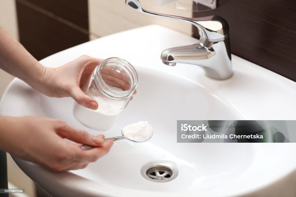 Woman using baking soda to unclog sink drain in bathroom, closeup Drain Stock Photo