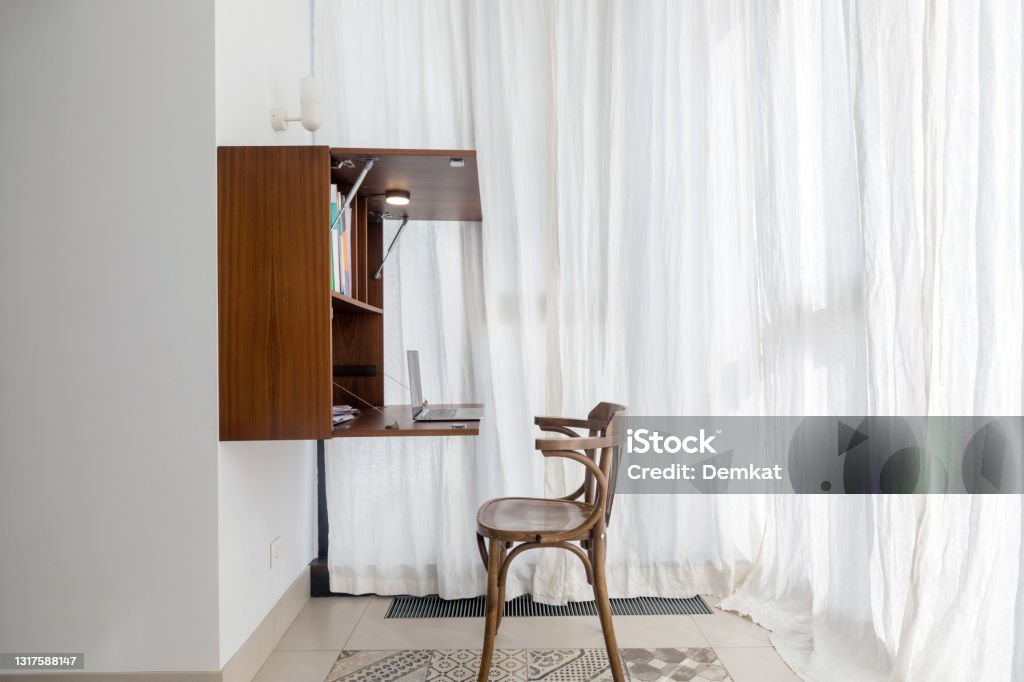 Minimalistic workplace in modern apartment bay window Convenient functional workplace with wooden chair placed near folding shelf with table hanging on wall in modern small area apartment in minimalist style Desk Stock Photo