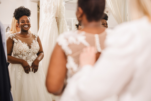 Asistente de tienda ayudando a la novia a meterse en el vestido de novia photo