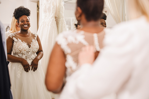 The future bride looks around the shop and tries on wedding dresses in the presence of her best friends. Lifestyle shopping concept, post-Covid-19 era