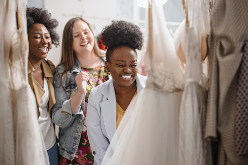 The future bride looks around the shop and tries on wedding dresses in the presence of her best friends. Lifestyle shopping concept, post-Covid-19 era