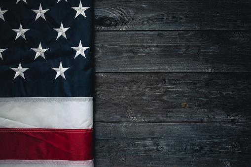 Flag of USA on dark wooden background.\nEmpty space provided for text placement for US celebrations such as: Memorial Day, Independence Day, etc.